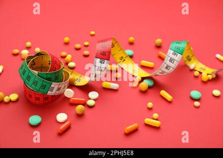 Many different weight loss pills and measuring tape on red background Stock Photo