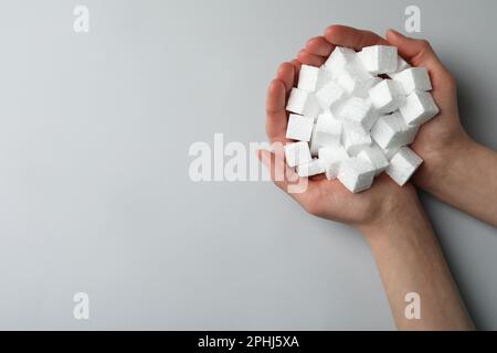 Woman with handful of styrofoam cubes on light grey background, top view. Space for text Stock Photo