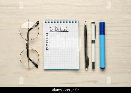 Notepad with unfilled To Do list, stationery and glasses on wooden table, flat lay Stock Photo