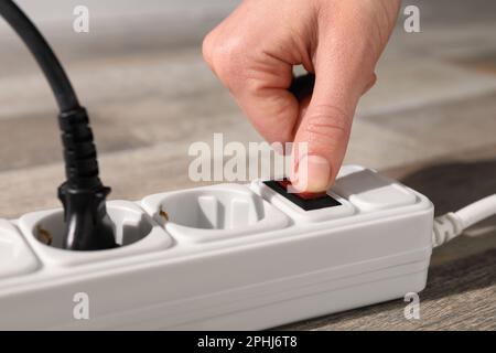 Man pressing power button of extension board on floor, closeup Stock Photo
