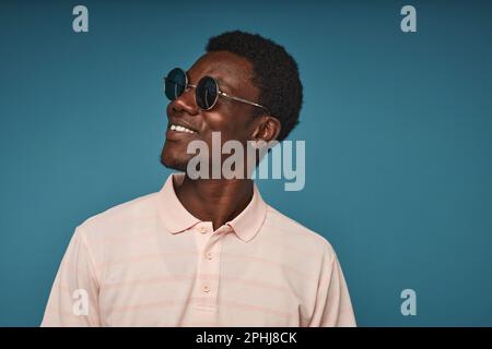 Minimal side view portrait of smiling black man wearing sunglasses against vibrant blue background, copy space Stock Photo