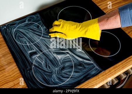 A man's hand in a protective yellow glove washes a ceramic stove. Close up. Stock Photo