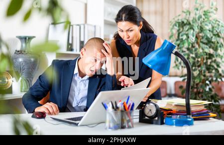 Upset office employe looking on laptop with disgruntled female manager Stock Photo