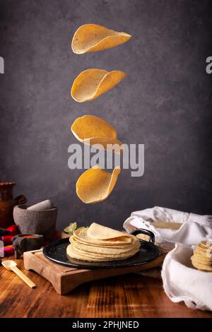 Corn tortillas falling on a Mexican griddle in a typical Mexican cuisine setting with a rustic wooden table and stone molcajetes. Stock Photo