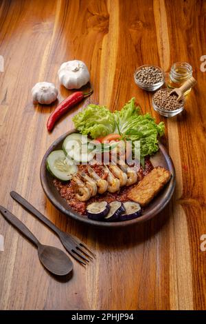 Deep fried shrimps or prawn with spicy chili sauce or sambal and eggplant in pottery plate on wooden table Stock Photo