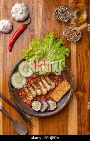 Deep fried shrimps or prawn with spicy chili sauce or sambal and eggplant in pottery plate on wooden table Stock Photo