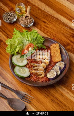 Deep fried shrimps or prawn with spicy chili sauce or sambal and eggplant in pottery plate on wooden table Stock Photo