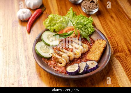 Deep fried shrimps or prawn with spicy chili sauce or sambal and eggplant in pottery plate on wooden table Stock Photo