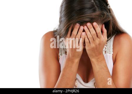 Tortured by her thoughts. Studio shot of a young woman covering her face against a white background. Stock Photo