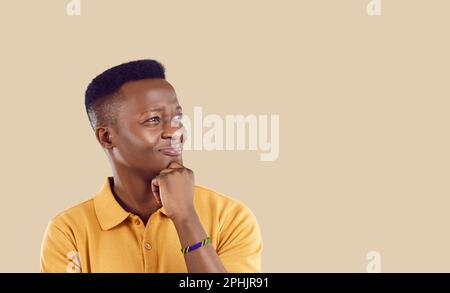 African American man with skeptical and doubtful expression looks at copy space on beige background Stock Photo