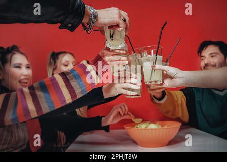 Diverse group of friends toasting with raised glasses at a pub with a red wall, focus on glasses, Caucasian and Asian individuals. Stock Photo