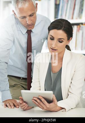 Collaborating has been their means to success. two coworkers using a digital tablet in an office. Stock Photo
