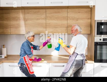 Mature couple doing chores together in kitchen, playing with spray bottles and having fun Stock Photo