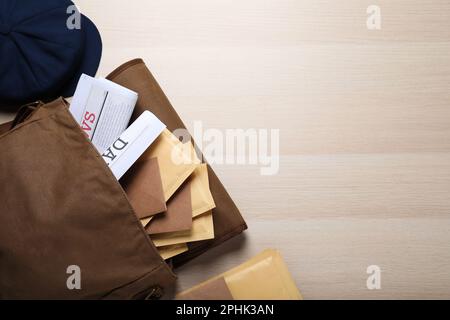 Brown postman's bag with envelopes, newspapers and hat on wooden table, flat lay. Space for text Stock Photo