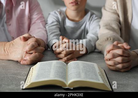 Boy and his godparents praying together at grey table, closeup Stock Photo