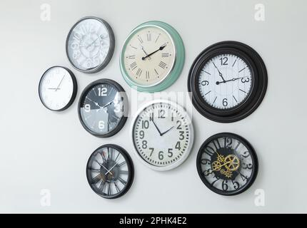 Many different clocks hanging on white wall. Stock Photo