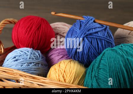 Clews of colorful knitting threads and crochet hook in wicker basket, closeup Stock Photo