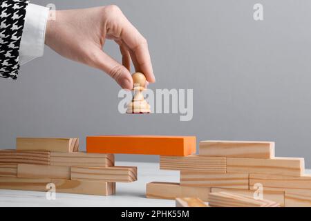 Businesswoman putting white pawn on bridge made of wooden blocks at table, closeup. Connection, relationships and deal concept Stock Photo