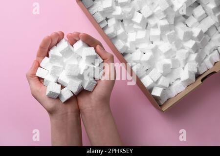 Woman with handful of styrofoam cubes on pink background, top view Stock Photo