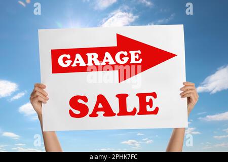 Woman holding sign with text GARAGE SALE against blue sky Stock Photo