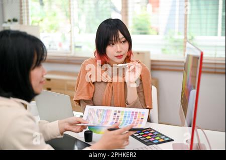 Two professional and talented Asian female graphic designers working on their new design project in the studio together. Stock Photo