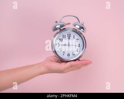 Female hand holding classic alarm clock on pink background. Close up of alarm clock in hand. Stock Photo