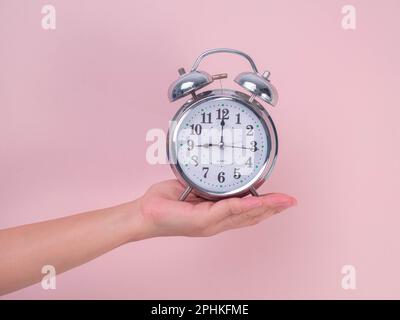 Female hand holding classic alarm clock on pink background. Close up of alarm clock in hand. Stock Photo