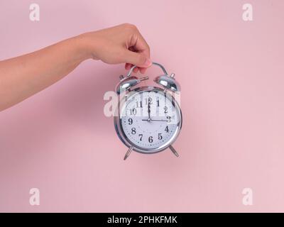 Female hand holding classic alarm clock on pink background. Close up of alarm clock in hand. Stock Photo