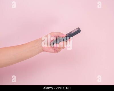 Hand pressing remote control isolated on pink background. Remote control in human hand. Stock Photo