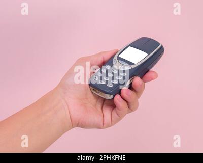 Close up hand holding mobile phone Nokia 3310 isolated on pink background. Female hand holding old used phone Nokia 3310. Stock Photo