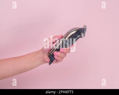 Close up hand holding electric hair clipper on pink background. Haircutting machine in hand. Stock Photo