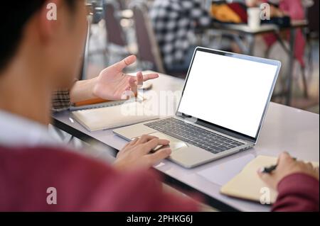 Close-up image of a young Asian male college student using laptop and doing a group project with his friends. laptop white screen mockup Stock Photo