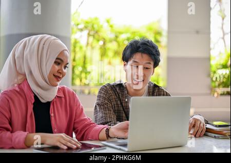 Two young Asian college students are looking at laptop screen, discussing and brainstorming on their school project together. diversity and friendship Stock Photo