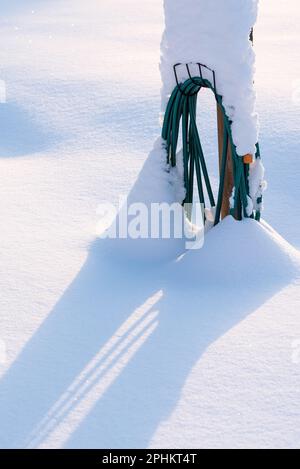 Coiled water hose buried in fresh newly fallen powder snow, winter in the garden. Stock Photo