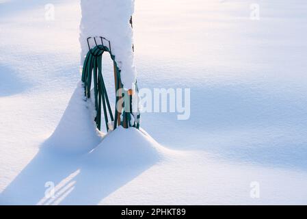 Coiled water hose buried in fresh newly fallen snow, winter in the garden. Stock Photo