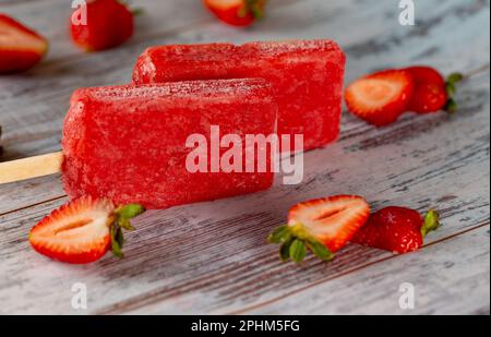 A close up of two strawberry-flavored popsicles surrounded by fresh strawberries Stock Photo