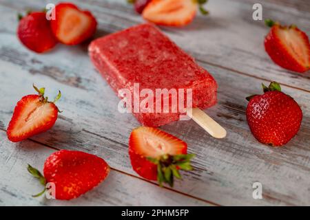 A close up of a strawberry-flavored popsicle surrounded by fresh strawberries Stock Photo