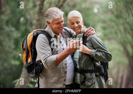 Phone, video call and elderly couple hiking in a forest, happy and smile while bonding on adventure. Active seniors, online and maps for man and woman Stock Photo