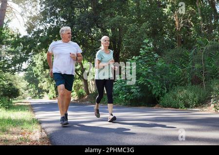 Fitness, senior and a couple running in a park for cardio, retirement exercise and movement. Happy, morning and an elderly man and woman jogging for Stock Photo