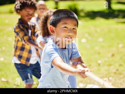 Fun, games and children playing tug of war together outdoor in a park or playground during summer. Friends, diversity and kids pulling a rope while Stock Photo