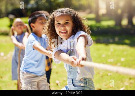 Funny, games and children playing tug of war together outdoor in a park or playground during summer. Friends, diversity and kids pulling a rope while Stock Photo