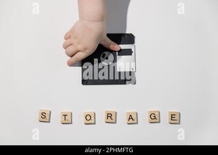 Child hand put floppy disk on white table. Backup and saving information concept. Memory Stock Photo