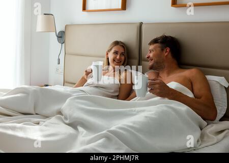 happy couple laying in bed and drinking morning coffee at home bedroom Stock Photo