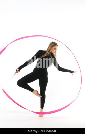 Girl gymnast in a black tight-fitting jumpsuit with a pink ribbon on a white background Stock Photo