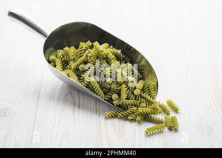 Mung bean fusilli pasta on a wooden background. Scoop with raw pasta and green mung bean. Gluten free pasta. Stock Photo