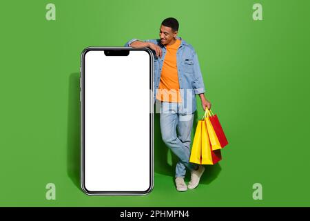 Full body photo curious young man go shopping using huge smartphone to shop online isolated on green color background Stock Photo