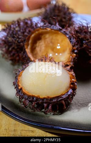 Tasty tropical exotic fruits, sweet ripe fresh peeled and unpeeled hairy rambutan southeast Asian fruits , close up Stock Photo