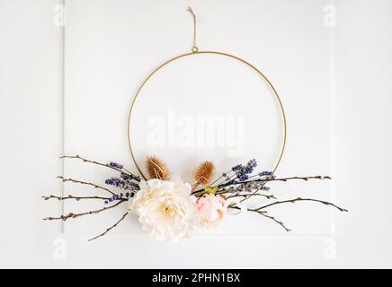 Handmade spring theme floral arrangement wreath hanging on home white door for decoration. Round metal hoop frame. Stock Photo