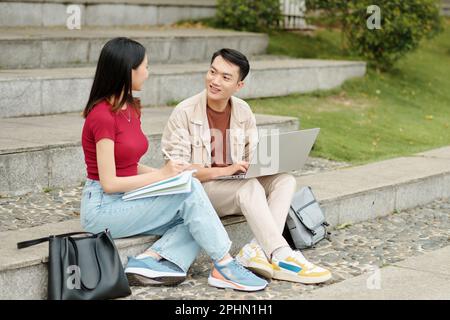 Cheerful students sitting onsteps on campus and discussing homework Stock Photo