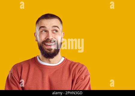 Portrait of happy smiling bearded brunet man in red sweatshirt looking aside on yellow background. Stock Photo